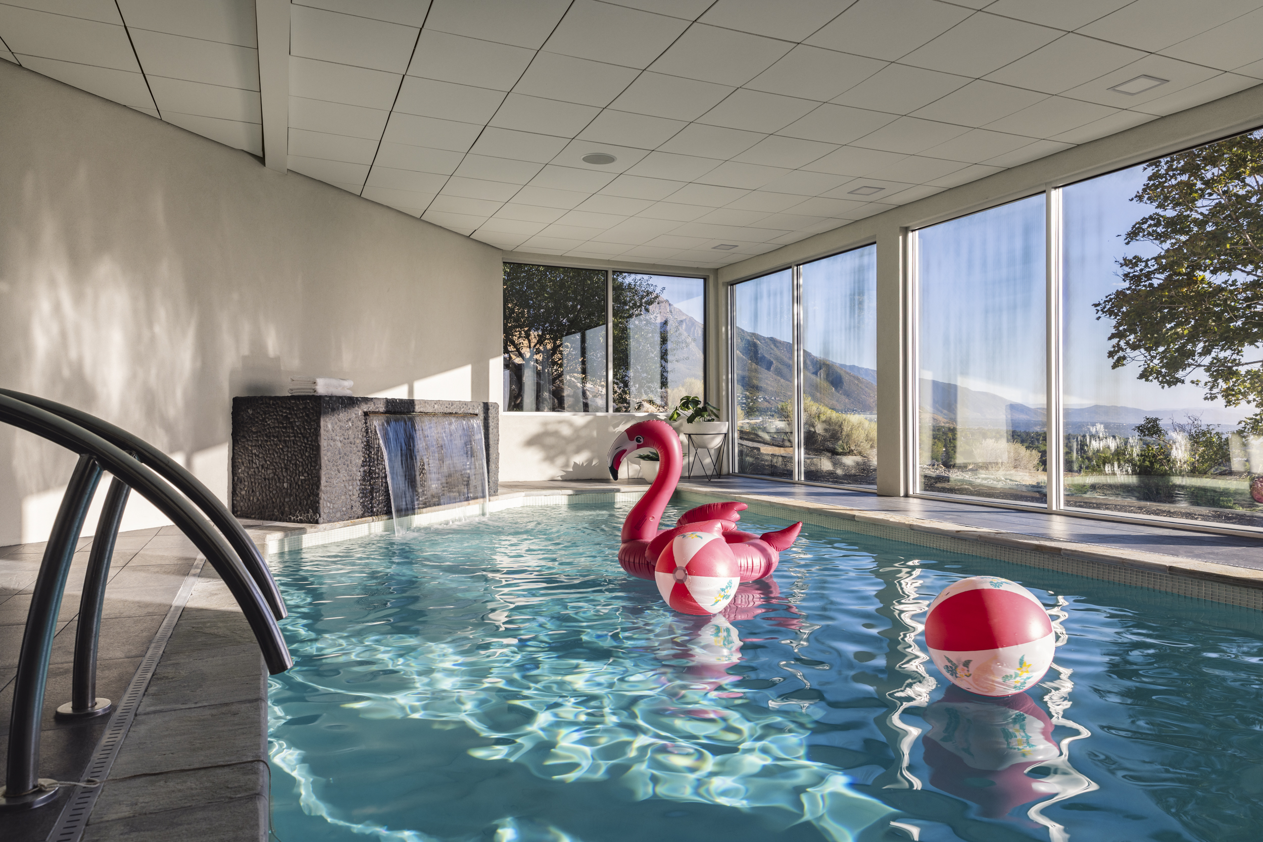 Sunlit indoor pool with a waterfall, pink float and mountain views
